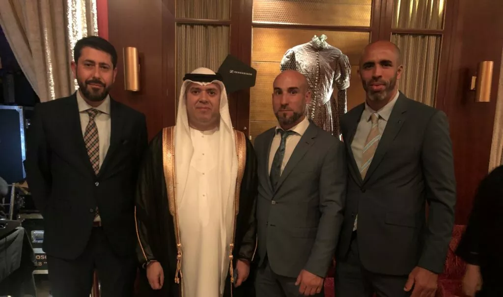 Cuatro hombres posan juntos en una recepción, uno de ellos con túnica blanca y pañuelo del Golfo