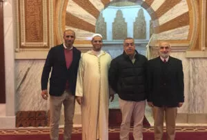 Cuatro hombres, uno con chilaba clara, posan ante el mihrab de mármol de la sala de oración