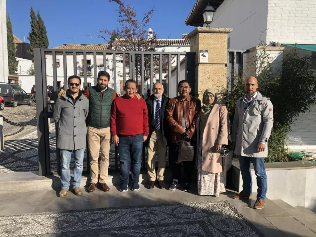 Siete personas posan ante la verja de entrada de la mezquita, con casas del Albaicín al fondo
