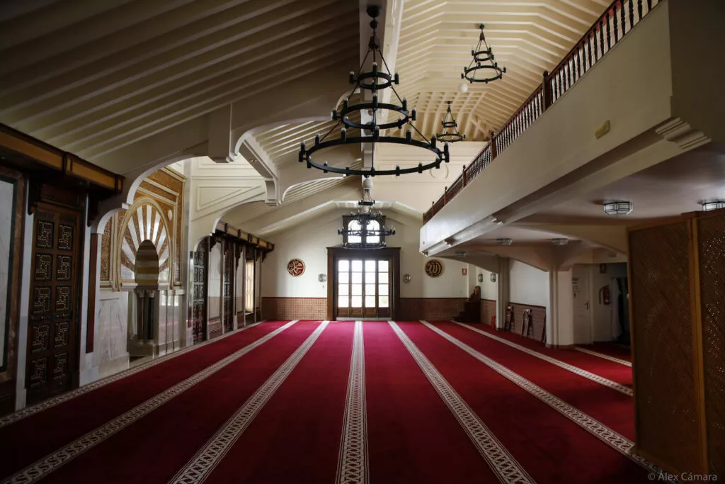 Vista longitudinal de la sala de oración, con las lámparas de forja, la galería superior y el mihrab al fondo