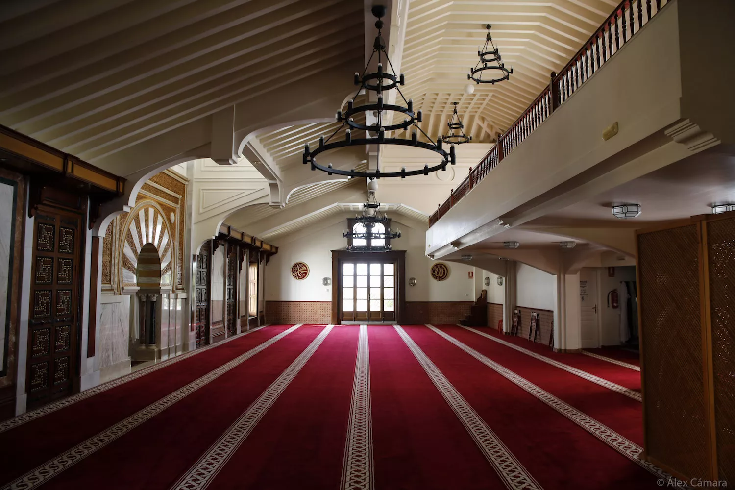 Vista longitudinal de la sala de oración, con las lámparas de forja, la galería superior y el mihrab al fondo