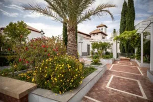 Jardín de la mezquita con palmera y flores y la torre del alminar con tejado de teja al fondo