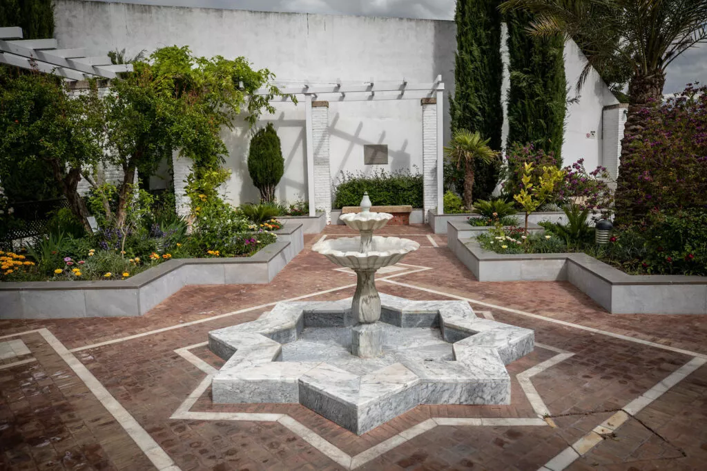 Patio ajardinado con la fuente de mármol en forma de estrella de ocho puntas y los parterres en flor