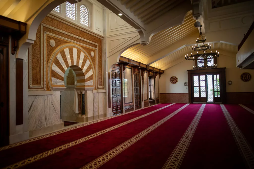 La sala de oración con el mihrab a la izquierda, las lámparas de forja y la puerta de entrada al fondo