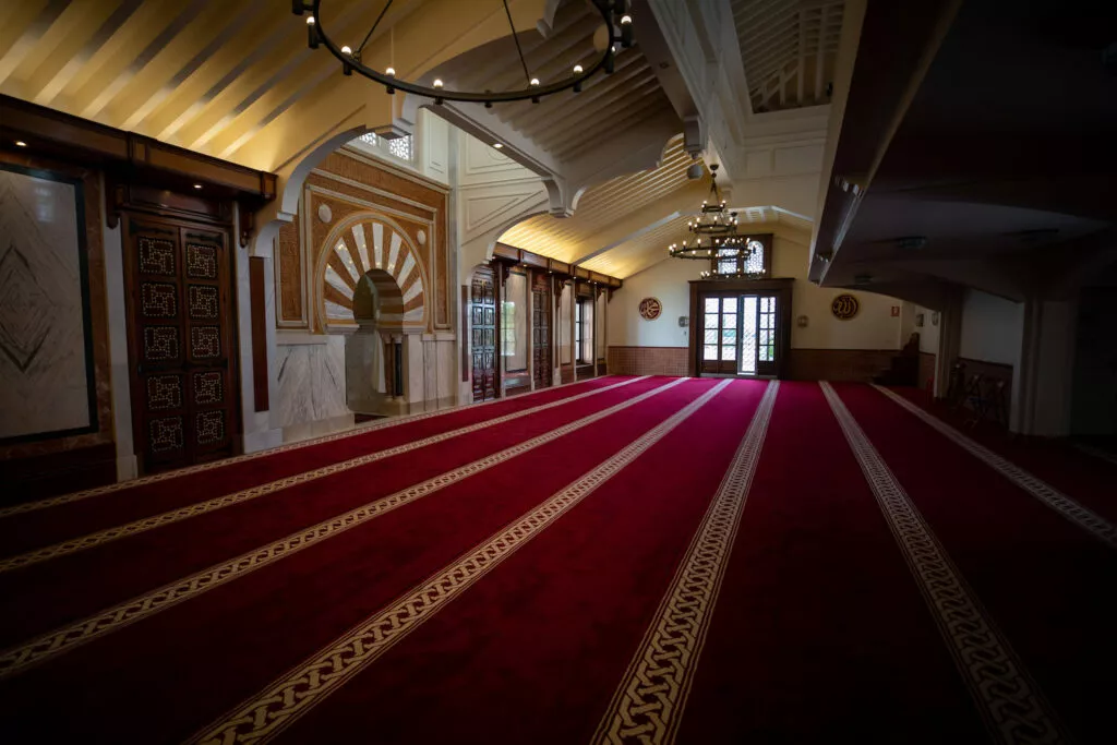 Vista a ras de alfombra de la sala de oración, con el mihrab a la izquierda y la puerta al fondo