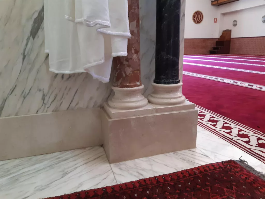 Columnas de mármol rojo y negro en el interior de la mezquita, con toallas colgadas y la alfombra roja al fondo