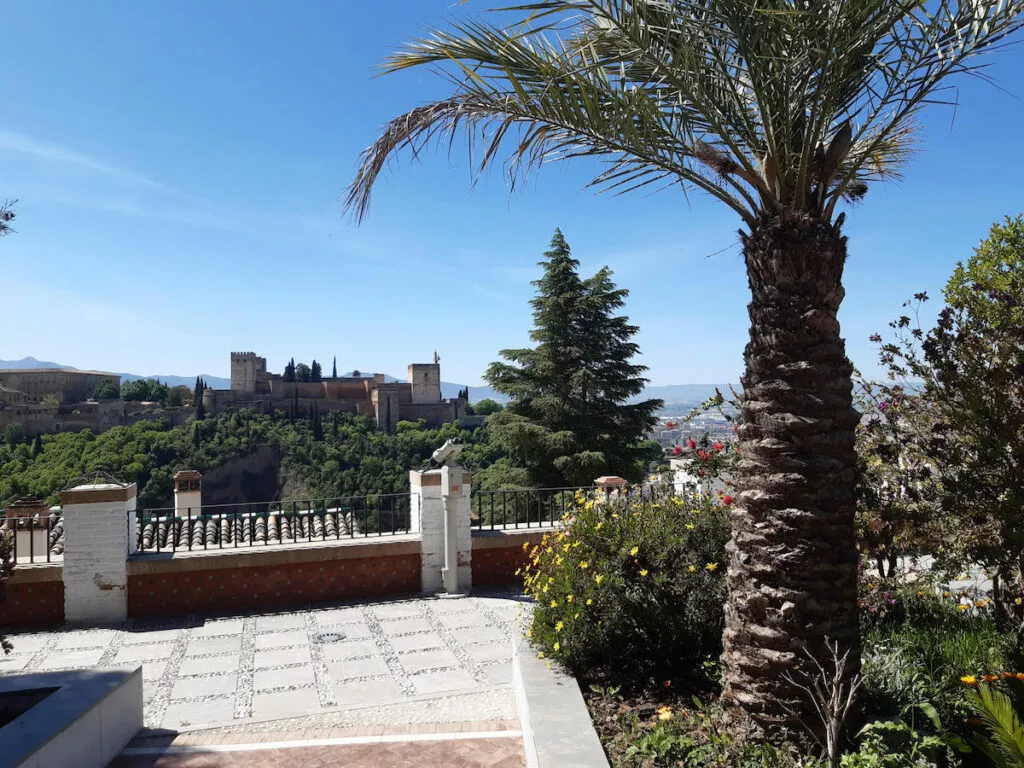 Terraza del mirador con una palmera en primer plano y la Alhambra al otro lado del valle