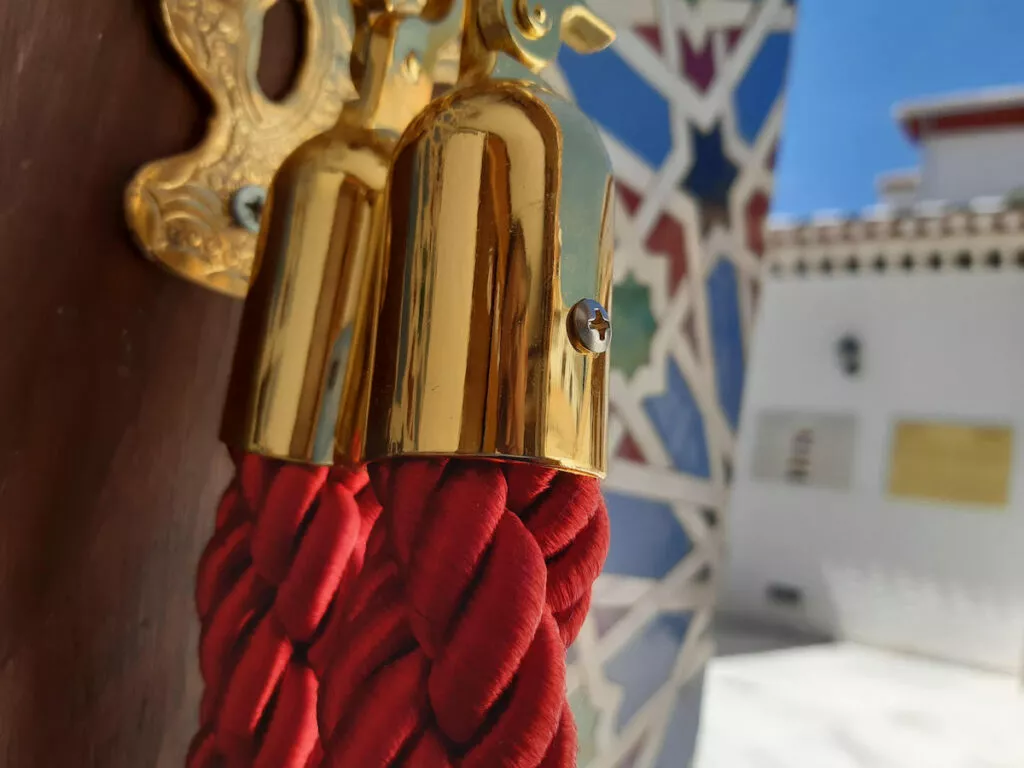 Detalle del cordón rojo con remate dorado que acota el paso, con la celosía de colores al fondo