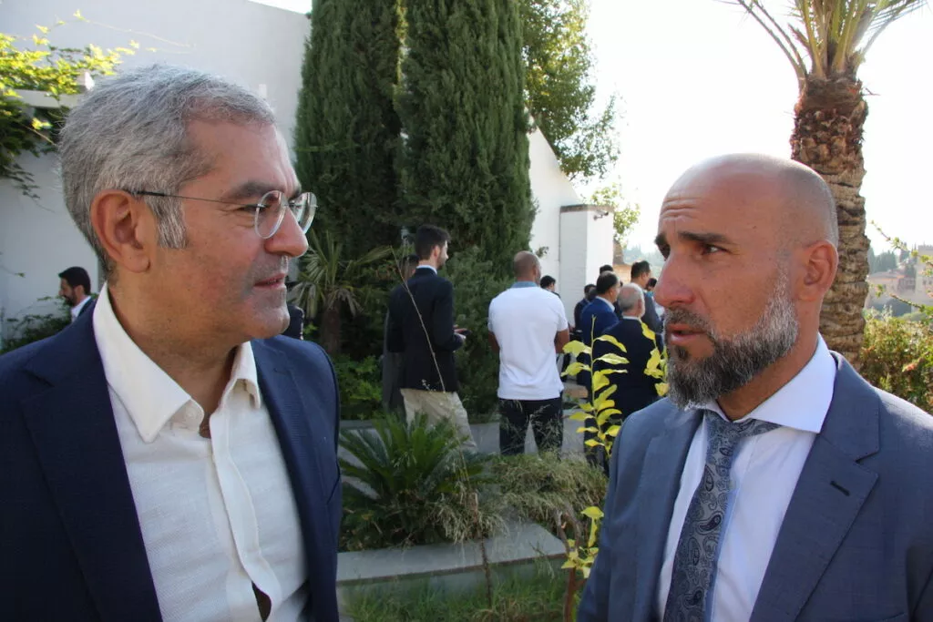 Dos asistentes conversan en el jardín durante la recepción, con más invitados al fondo