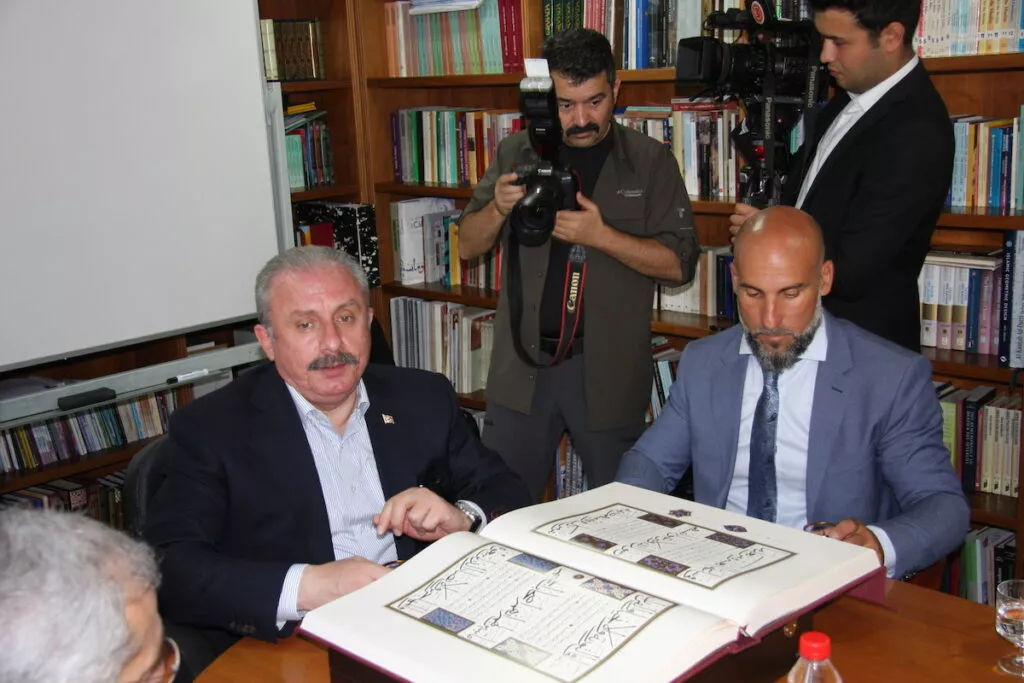 Dos personas examinan un facsímil de un manuscrito coránico iluminado en la biblioteca, ante los fotógrafos
