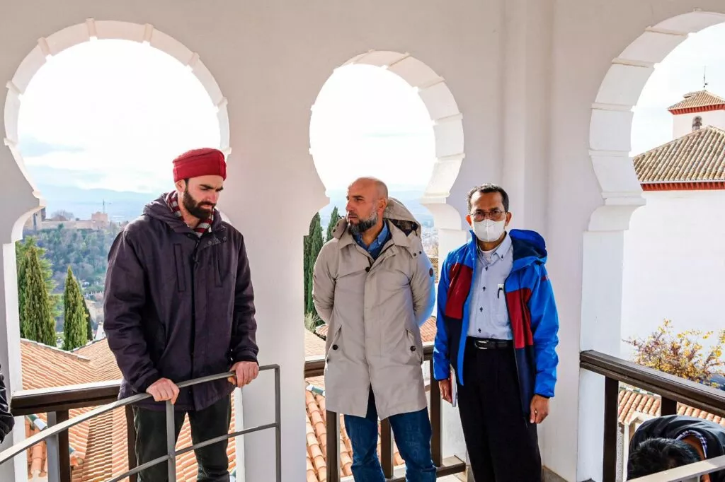 Tres visitantes conversan en la galería del mirador, con los tejados del Albaicín al fondo