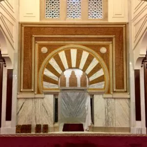 Mihrab de la mezquita con arco de herradura, yeserías doradas y mármol blanco sobre alfombra roja