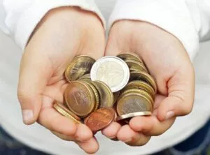 Manos infantiles sostienen un puñado de monedas de euro sobre un fondo desenfocado