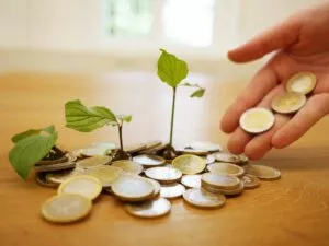 Monedas de euro con brotes verdes creciendo entre ellas y una mano dejando caer más monedas
