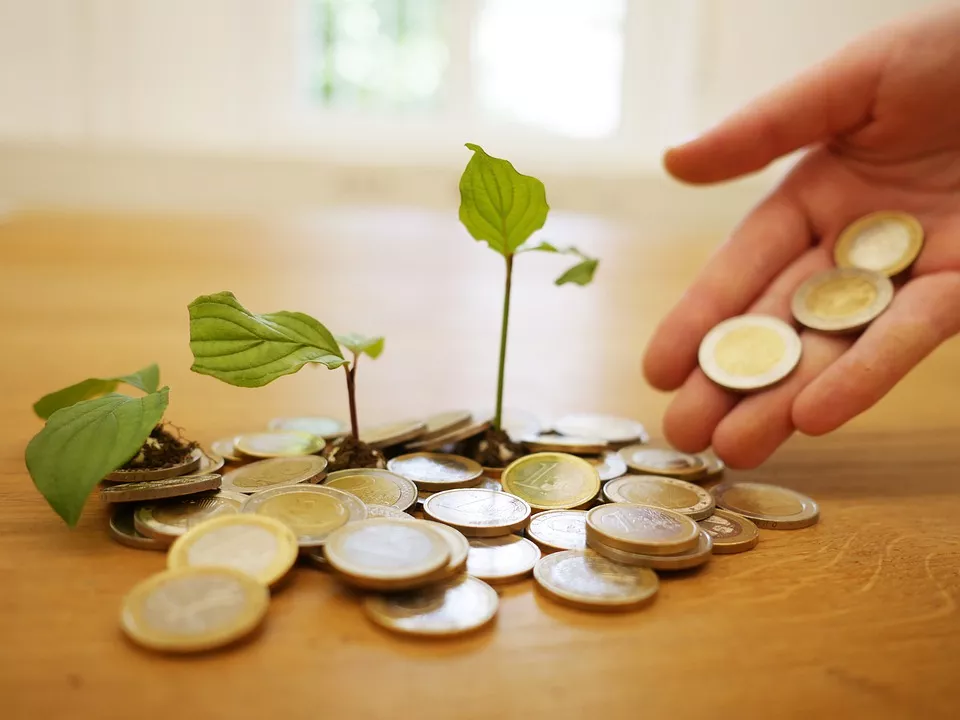 Monedas de euro con brotes verdes creciendo entre ellas y una mano dejando caer más monedas