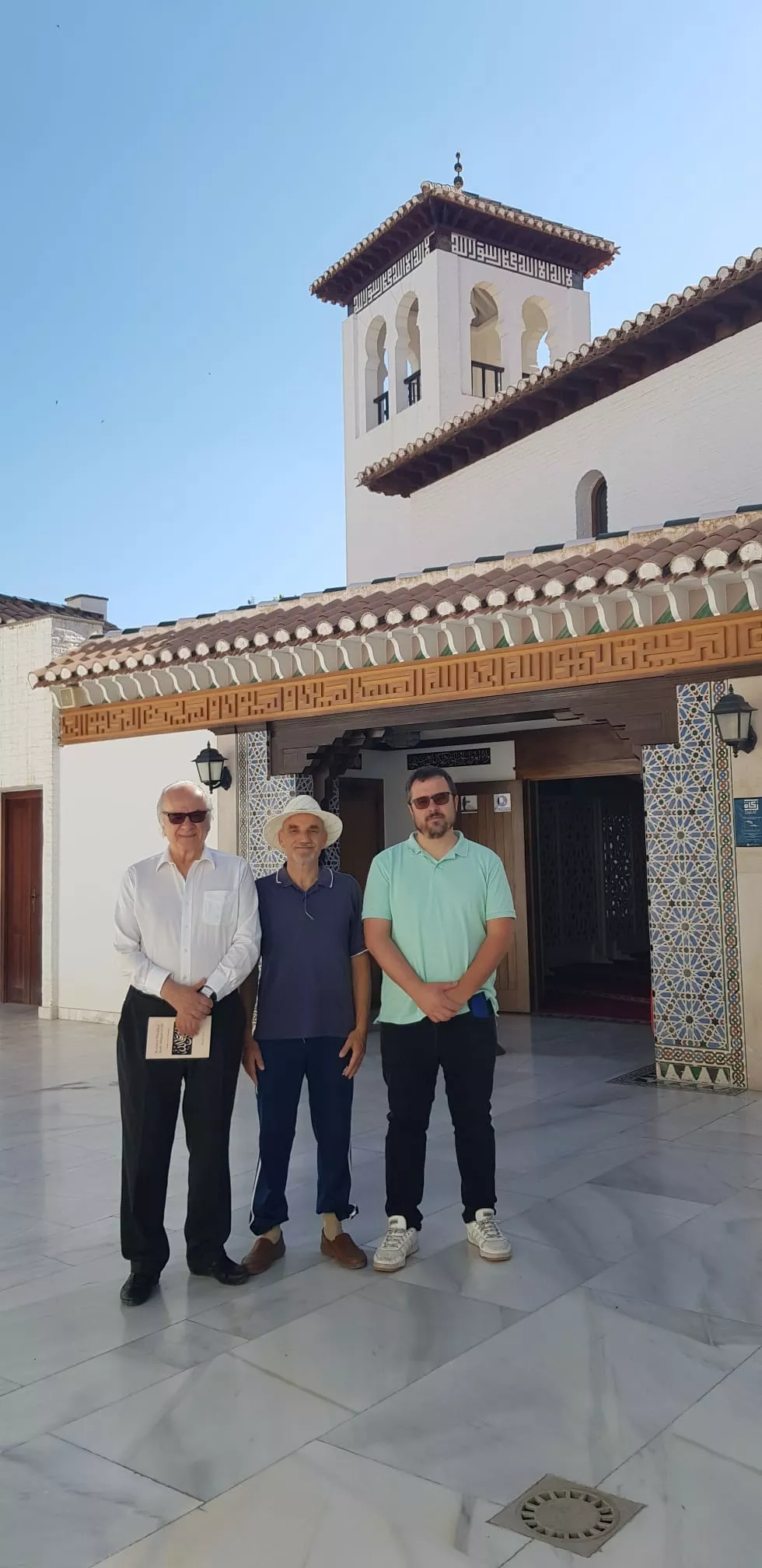 Tres visitantes posan ante el porche de entrada de la mezquita, con el alminar al fondo