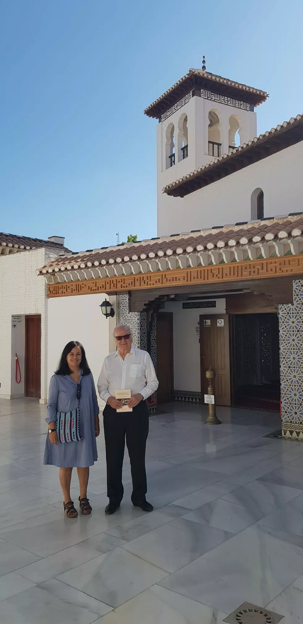 Dos visitantes posan ante la entrada de la mezquita, uno de ellos con un libro en la mano