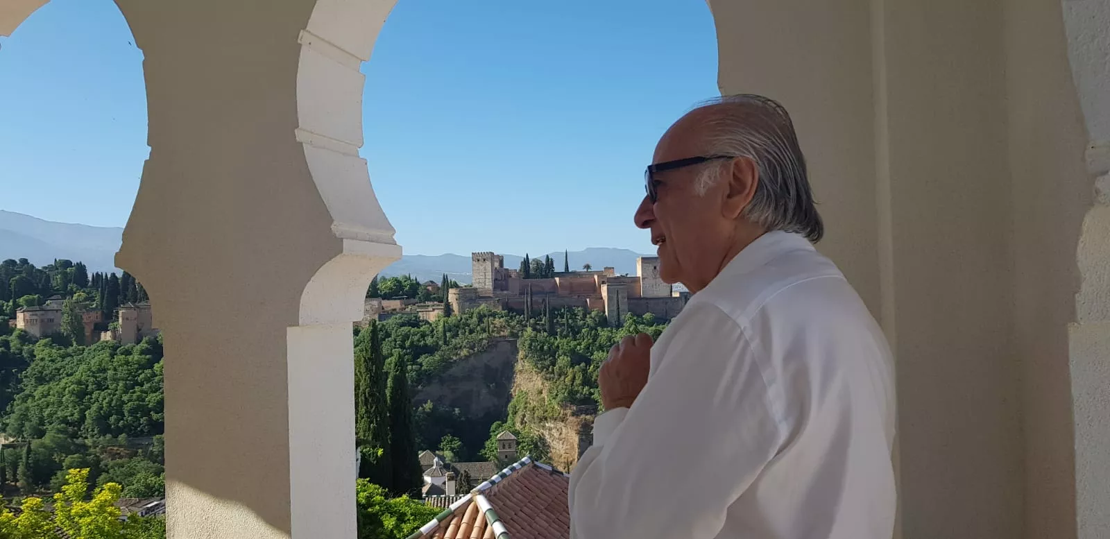 Un hombre mayor de camisa blanca contempla la Alhambra desde un arco de herradura de la mezquita