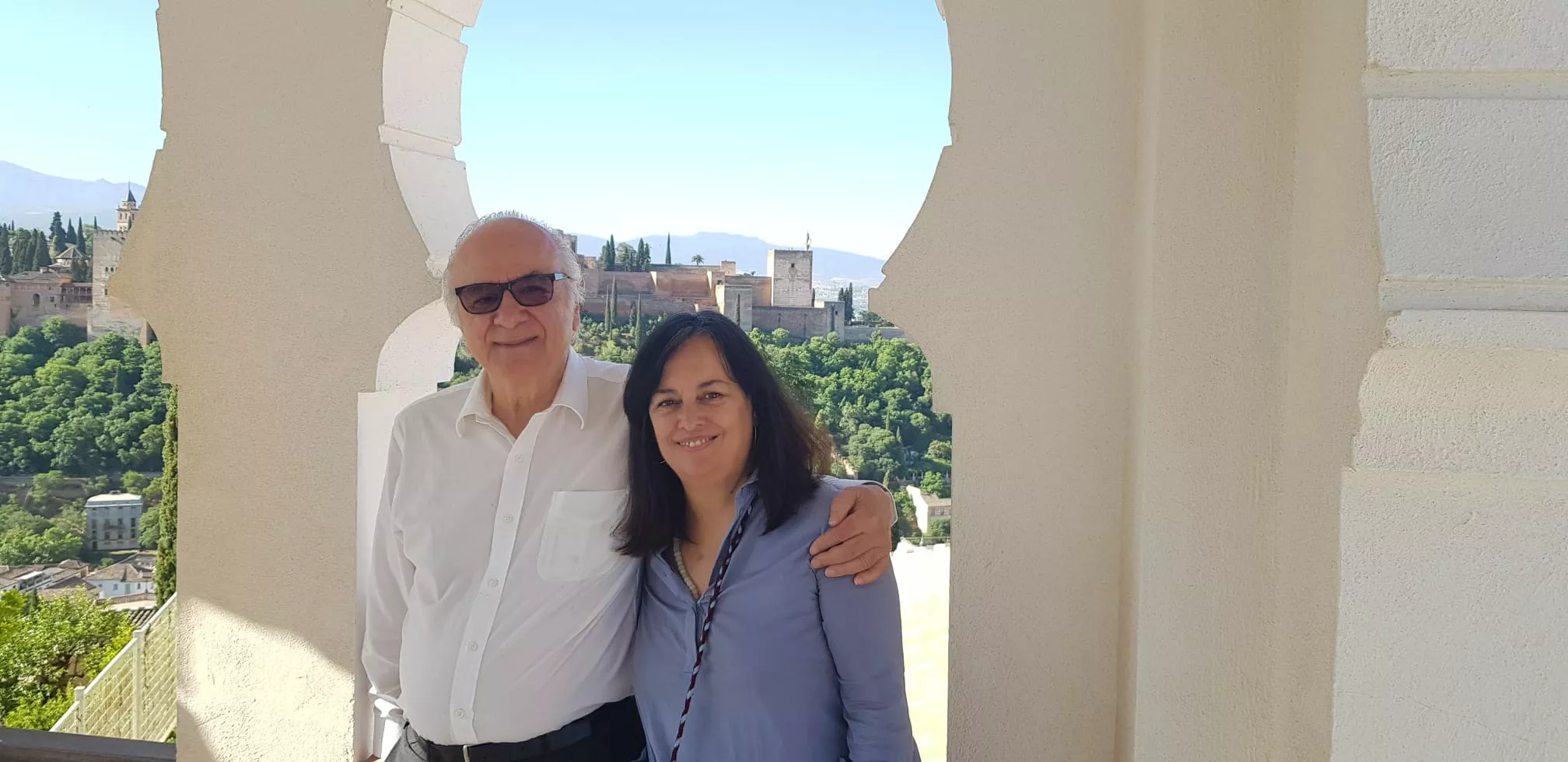 Dos visitantes posan en el mirador, con la Alhambra entre los arcos al fondo