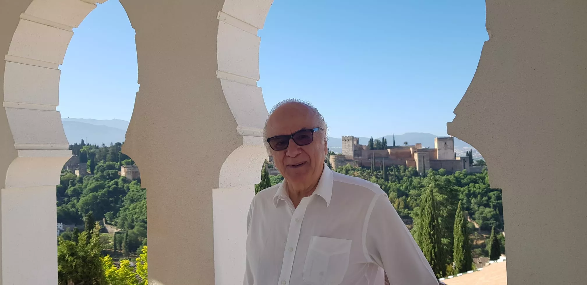 Un visitante sonríe bajo los arcos del mirador, con la Alhambra al fondo
