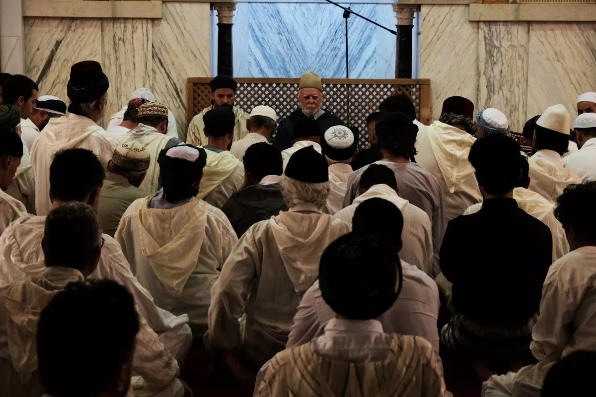 Fieles vestidos de blanco sentados en la sala de oración escuchando al orador ante el mihrab