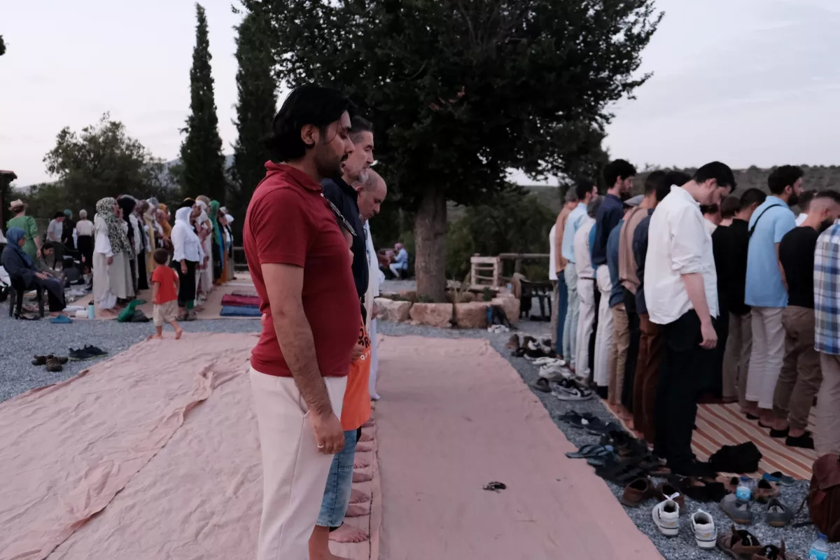 Filas de fieles en pie para la oración al aire libre sobre esteras, al atardecer