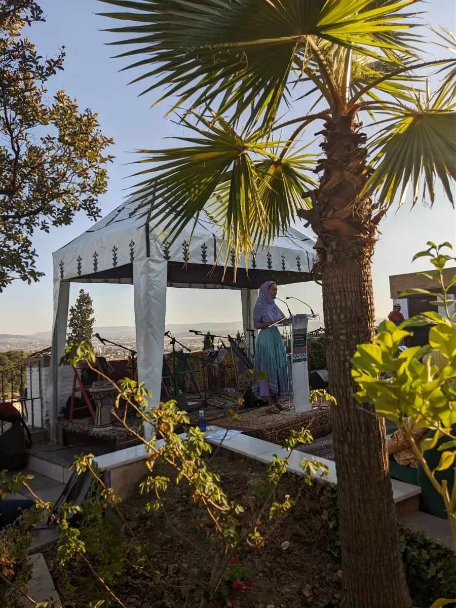 Mujer leyendo en un atril bajo una jaima blanca en la terraza, con la vega de Granada al fondo