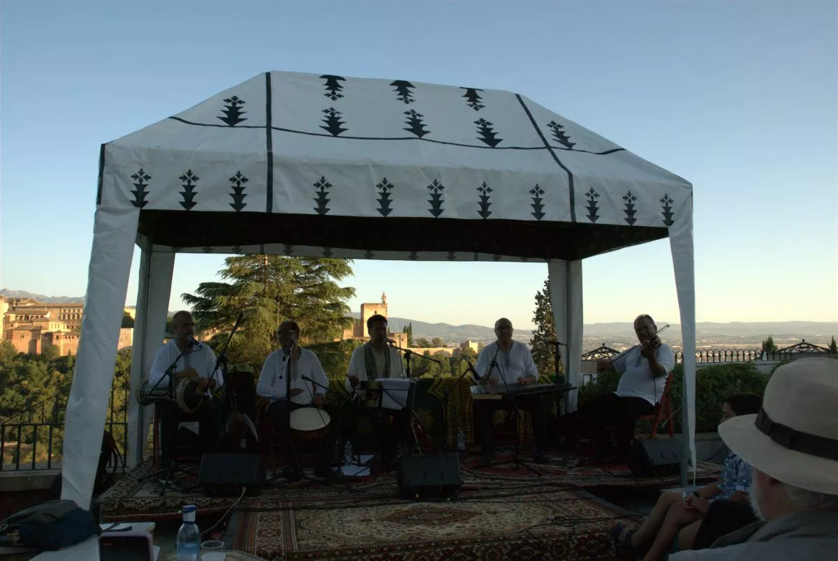 Grupo musical tocando bajo una jaima blanca en el jardín, con la Alhambra al fondo