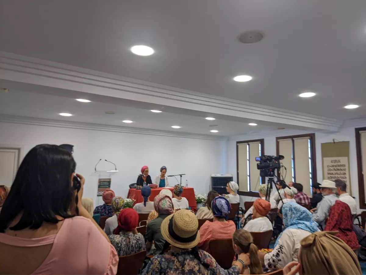 Dos ponentes en la mesa durante el encuentro de mujeres, con el público sentado y una cámara grabando