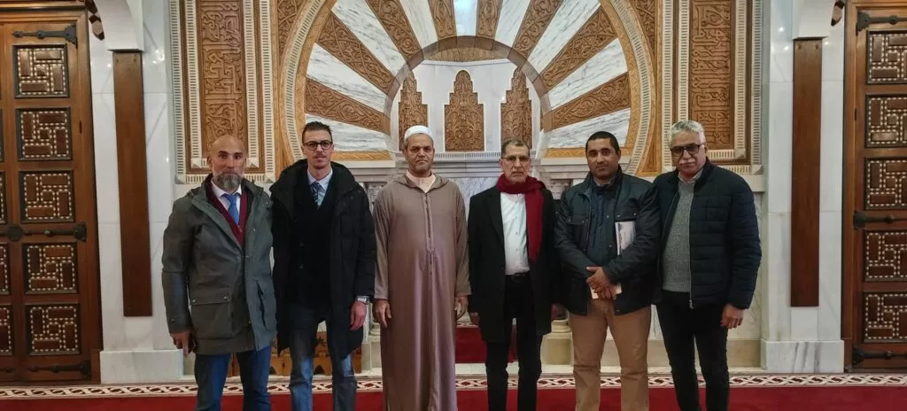 Seis hombres posando ante el mihrab de mármol y madera tallada de la sala de oración