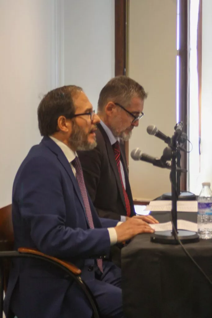 Dos ponentes con traje leen sus textos ante los micrófonos en la mesa de las jornadas