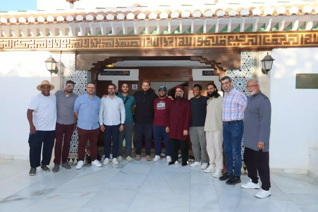 Grupo de trece visitantes posando ante la puerta de madera tallada y los azulejos de la mezquita