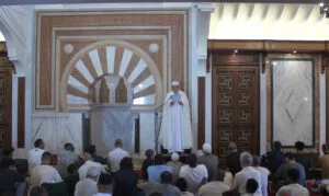 El imam, vestido de blanco, lee la jutba ante el mihrab con los fieles sentados en la sala