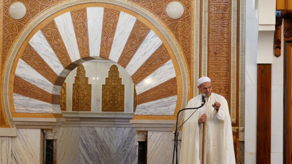 El imam de blanco levanta el dedo mientras predica ante el arco de herradura del mihrab