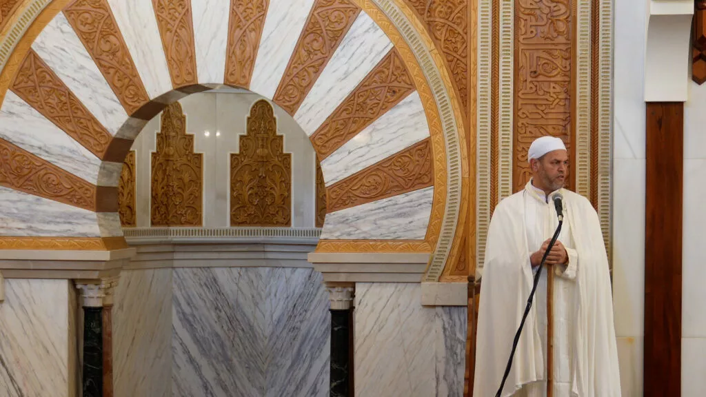 El jatib, con chilaba y turbante blancos, da la jutba ante el micrófono junto al mihrab