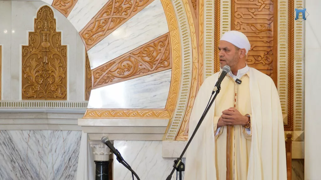 Jatib con chilaba clara y turbante blanco habla ante el micrófono junto al mihrab de mármol