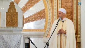 Jatib con chilaba clara y turbante blanco habla ante el micrófono junto al mihrab de mármol